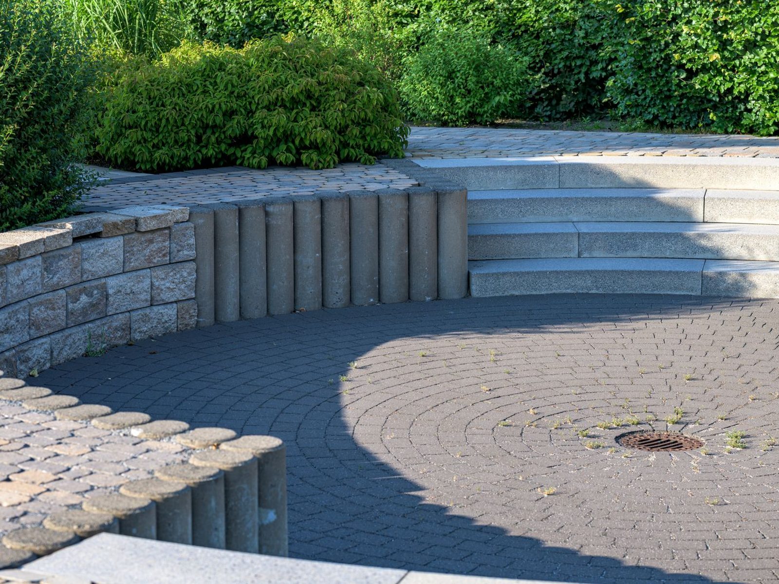 Runde Pflasterfläche mit Palisaden, Natursteinmauer und Blockstufen